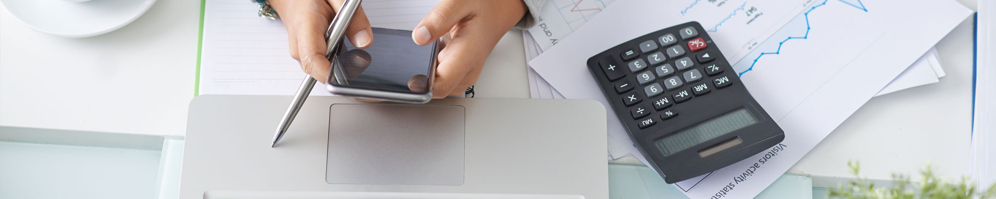 person checking their smart phone with a laptop and calculator nearby