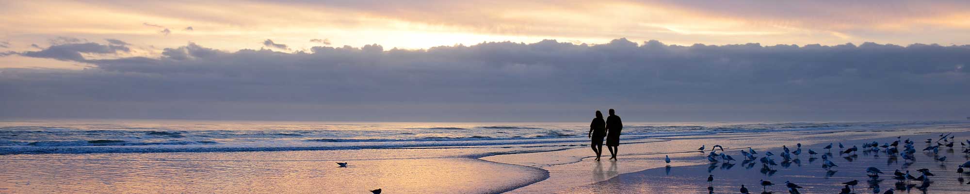 two people walking in the tide on a beach at sunset